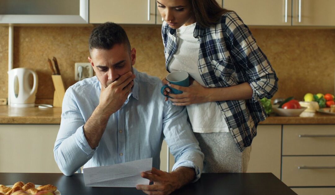Pareja preocupada leyendo junta la carta de negación de un reclamo de seguro en la cocina de su casa