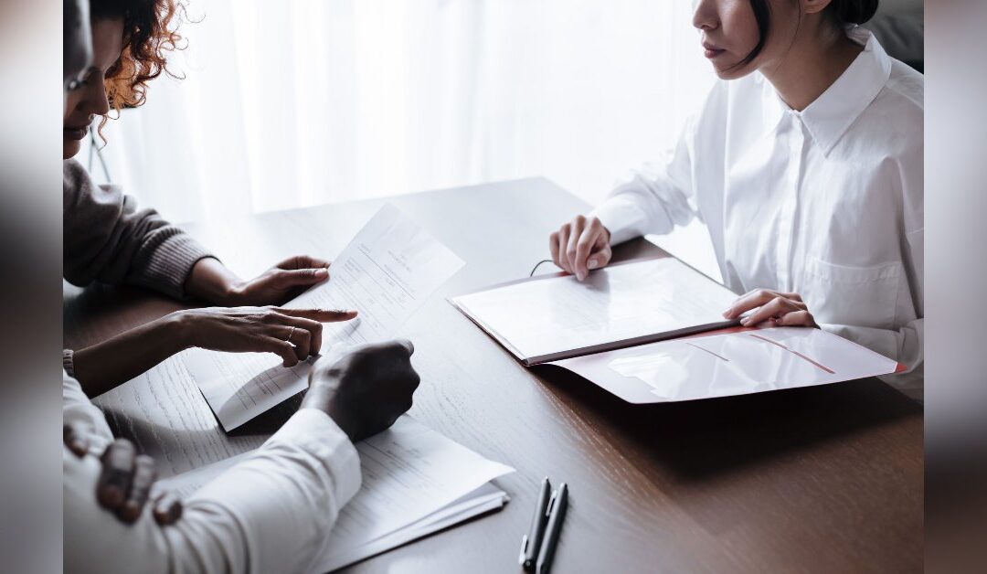 Couple at a table going over insurance claim paperwork while deciding who should handle their claim